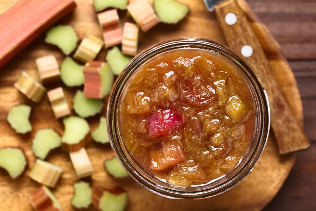 borcan cu dulceata de rubarba pe tocator din lemn cu bucati de rubarba
