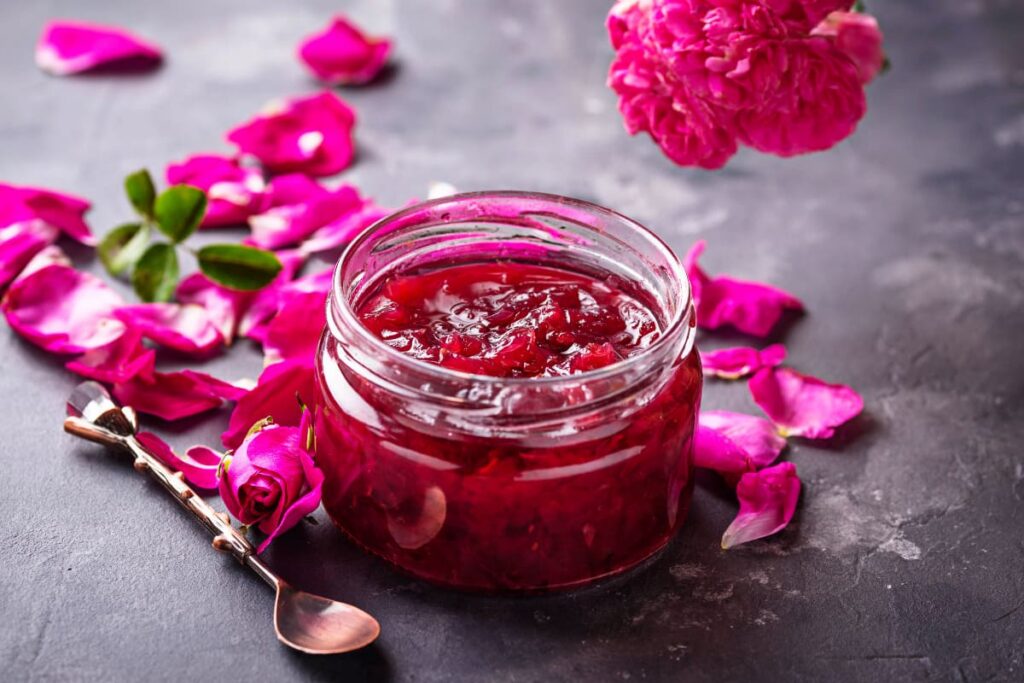 borcan cu dulceata de trandafiri pe masa alaturi de petale de trandafiri