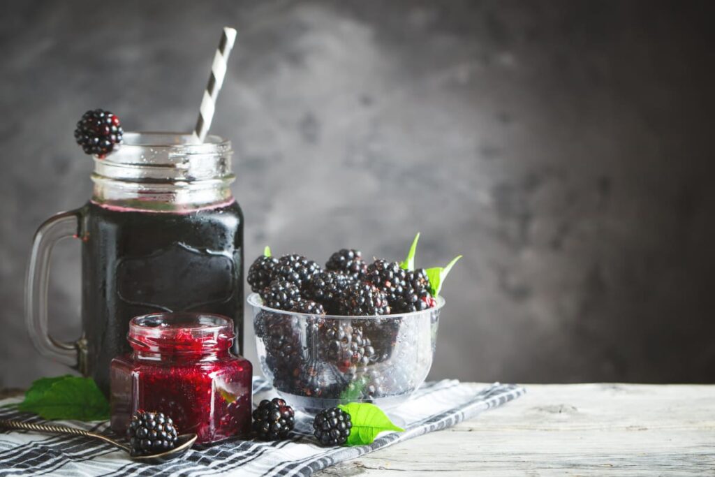 borcan cu sirop de mure alaturi de recipient cu mure si dulceata de mure pe masa