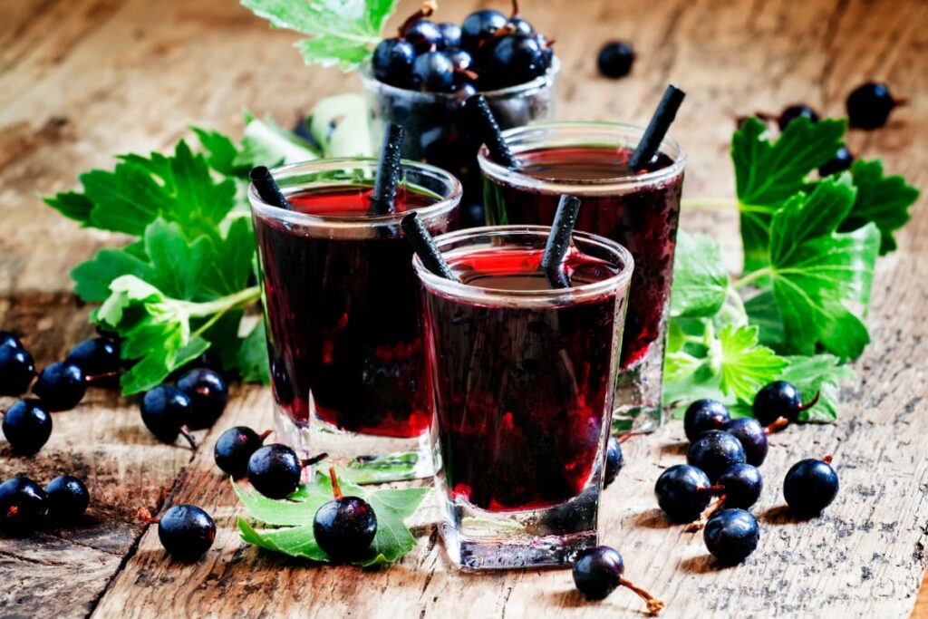 pahare mici cu alcool si sirop de coacaze negre pe masa rustica din lemn