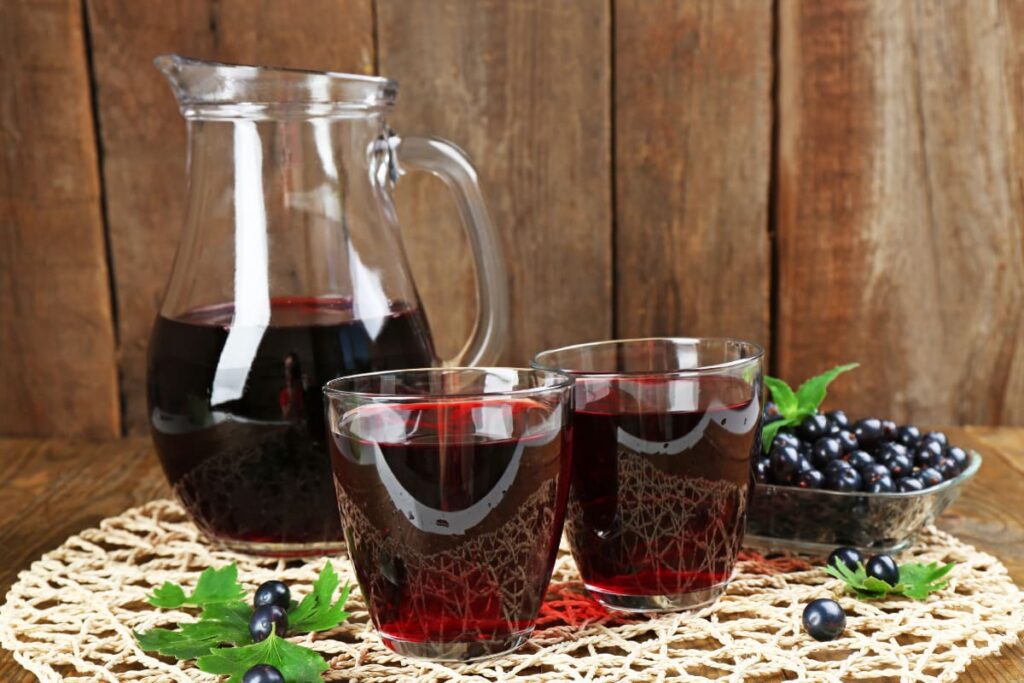 pahare si carafa cu sirop de coacaze negre pe masa rustica cu broderie